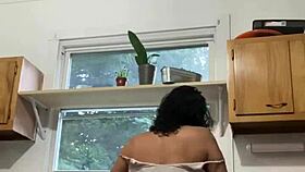 Latina milf enjoys washing dishes in the kitchen with a smile.
