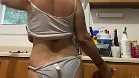 Latina milf enjoys washing dishes in the kitchen with a smile.