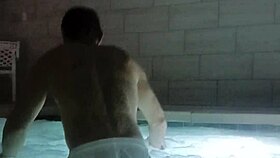 A muscular man soaks in public jacuzzi.